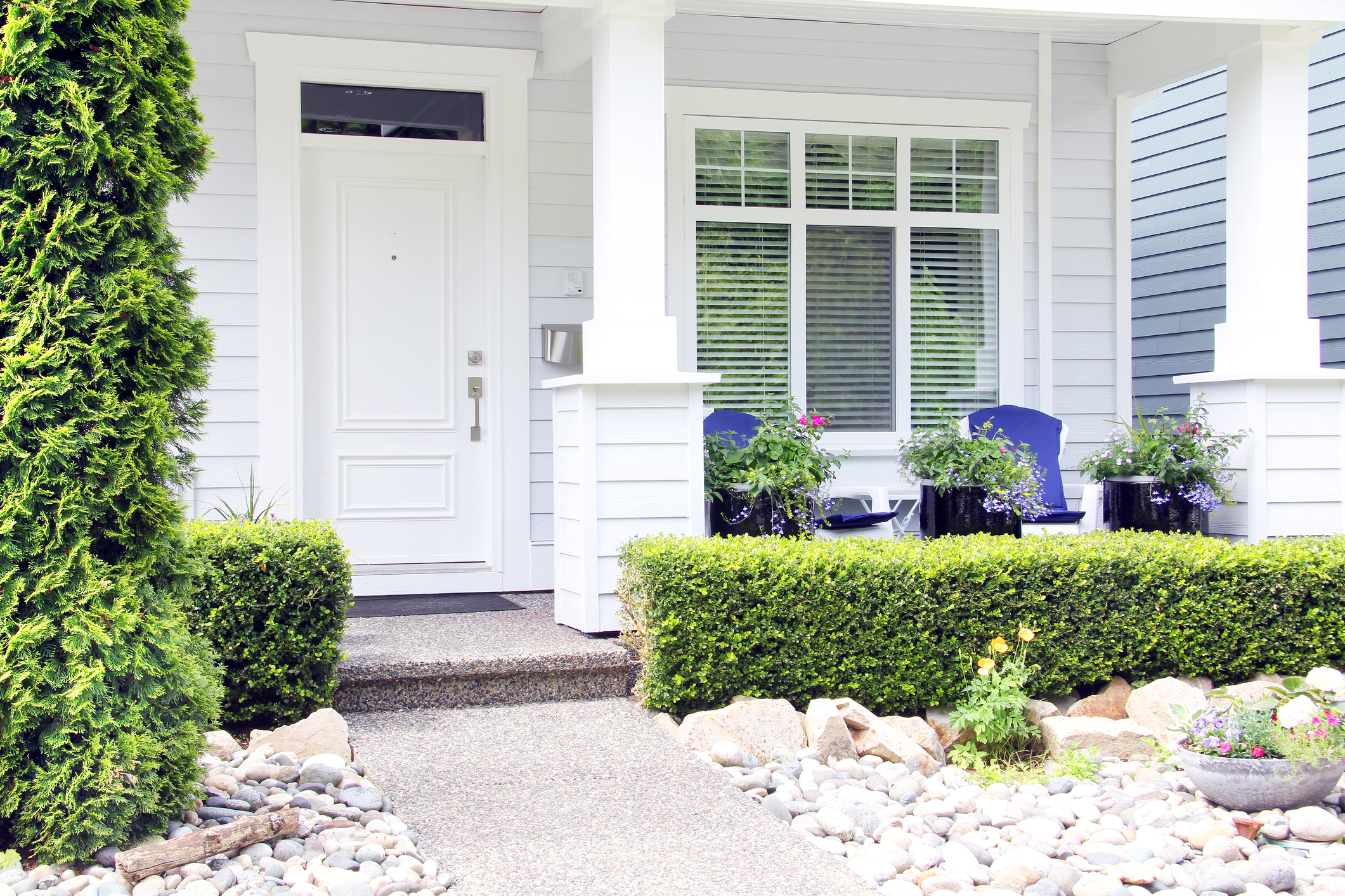 Front porch with white entry door, large window, blue chairs, and potted flowers, creating a clean and welcoming curb appeal.
