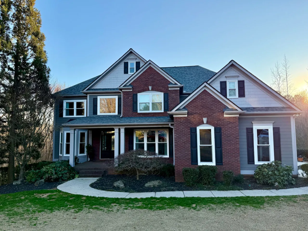 Beautiful two-story brick home with new energy-efficient windows, black shutters, and a covered front porch in a landscaped yard.